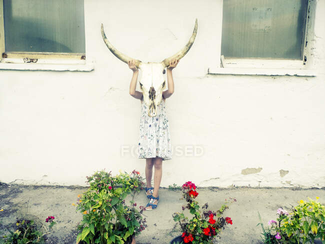 Chica de pie en un jardín sosteniendo un cráneo de búfalo en frente de su cara, Hungría - foto de stock