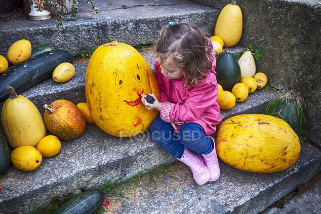 Chica sentada en un paso dibujando una cara sonriente en una calabaza de Halloween, Polonia - foto de stock