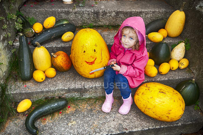 Chica sentada en un escalón sosteniendo un cuchillo listo para hacer una linterna Jack-o-Halloween, Polonia - foto de stock