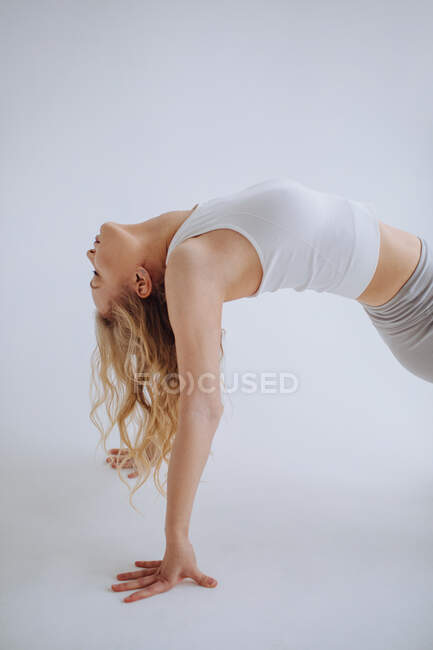 Vista lateral de una mujer en ropa deportiva casual haciendo un backbend - foto de stock