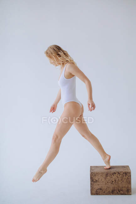 Female gymnast in a white leotard stepping down off a wooden block — Stock Photo