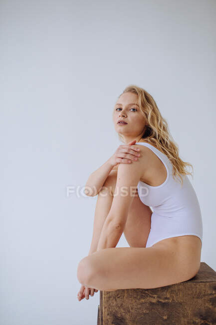 Ginasta feminina em um collant branco sentado em um bloco de madeira — Fotografia de Stock