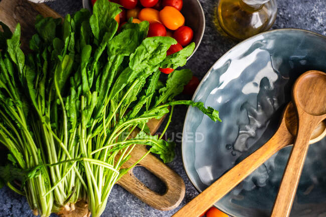 Cohete fresco, tomates y aceite de oliva junto a un plato con ensaladas - foto de stock