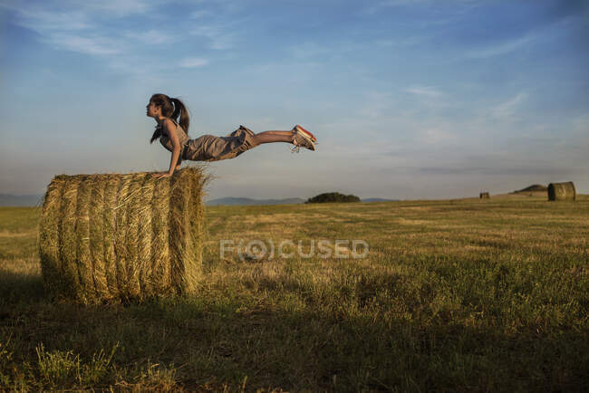 Uma adolescente balançando as mãos no ar em um fardo de feno em um campo, Bulgária — Fotografia de Stock