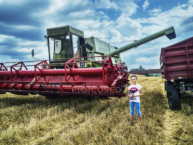 Улыбающаяся девушка, стоящая на пшеничном поле возле комбайна, Польша — стоковое фото