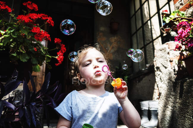 Fille debout devant une maison soufflant des bulles de savon, Pologne — Photo de stock