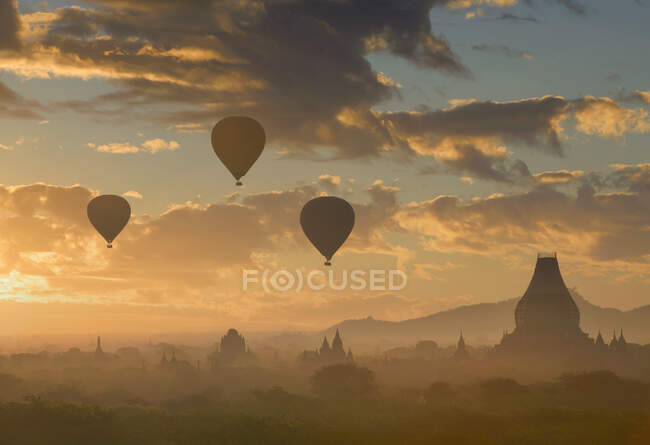 Silhouette von Heißluftballons, die bei Sonnenuntergang über Tempel fliegen, Bayan, Myanmar — Stockfoto