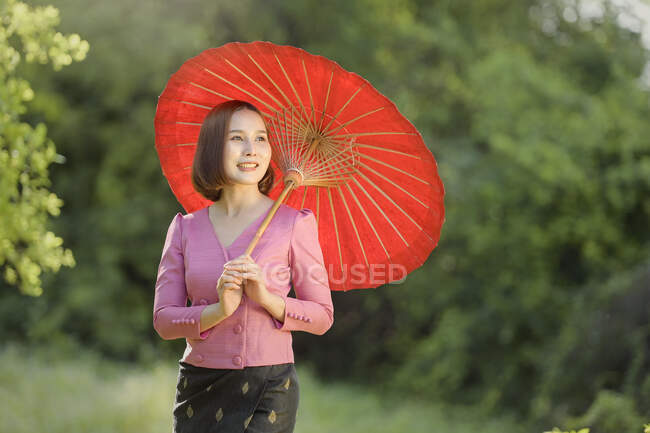 Портрет улыбающейся женщины, стоящей в саду с зонтиком в руках, Таиланд — стоковое фото