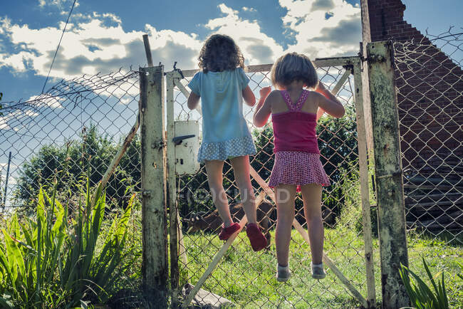 Rear view of two girls climbing on a metal fence, Poland — Stock Photo