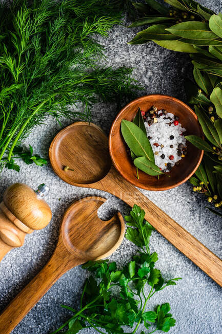Rock salt, peppercorns, bay leaves, dill and parsley with salad serving spoons — Stock Photo