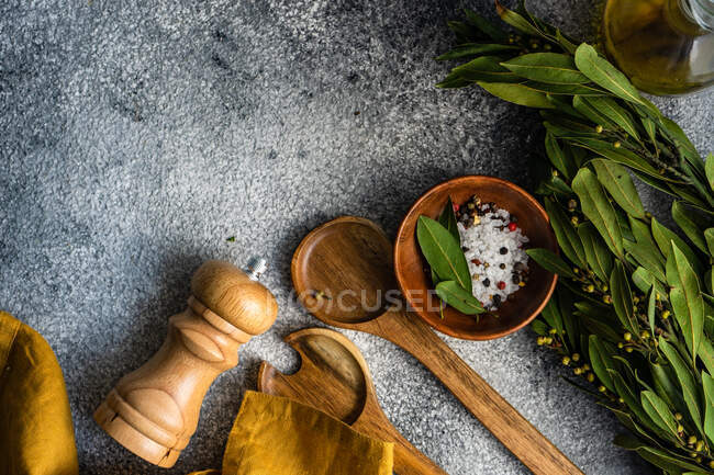 Sal de roca, granos de pimienta, hojas de laurel y aceite de oliva con cucharas para servir ensaladas - foto de stock