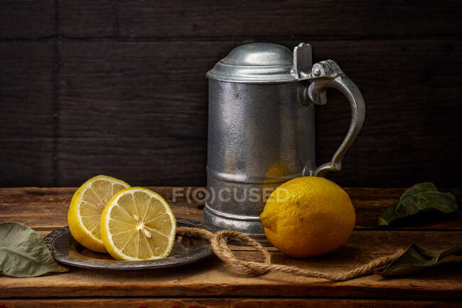 Лимоны рядом с металлическим танкардом на деревянном столе — стоковое фото