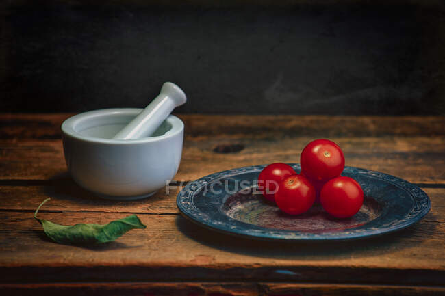 Tomates de cereja em uma chapa ao lado de um morteiro e pilão em uma mesa de madeira — Fotografia de Stock