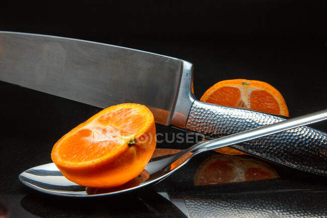 Primo piano di un mandarino dimezzato su un cucchiaio con un coltello — Foto stock