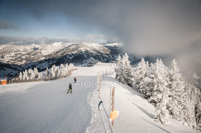 Vista trasera de dos esquiadores esquiando por una montaña, Zell am See, Salzburgo, Austria - foto de stock