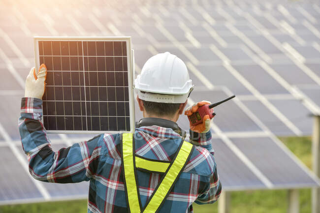Rear view of an engineer at a solar farm carrying a solar panel, Thailand — Stock Photo