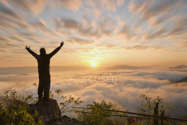Silhueta de um homem de pé em uma montanha com os braços estendidos ao nascer do sol, Tailândia — Fotografia de Stock