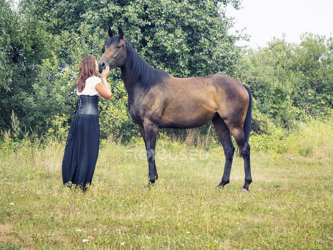 Donna in piedi in un campo baciare un cavallo, Polonia — Foto stock