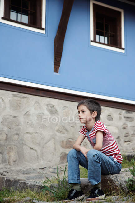 Niño sentado en las escaleras fuera de una casa, Bulgaria - foto de stock