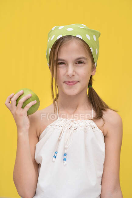 Retrato de una chica sonriente con un pañuelo verde de lunares sosteniendo una manzana verde - foto de stock