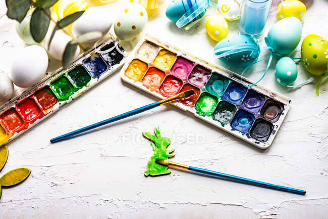 Two paint brushes, a palette with watercolour paints and Easter eggs — Stock Photo