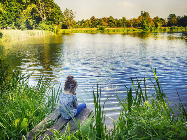 Vista trasera de una chica sentada junto a un lago, Polonia - foto de stock