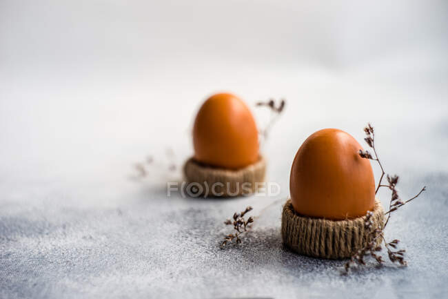 Dos huevos cocidos en tazas de huevo junto a flores secas - foto de stock
