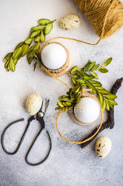 Eggs in egg cups and quail eggs with boxwood leaves, string and scissors — Stock Photo