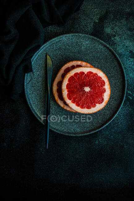 Спелые розовые ломтики грейпфрута на черной тарелке — стоковое фото