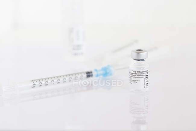 Vial de la vacuna contra el Coronavirus y jeringa sobre una mesa en una clínica - foto de stock