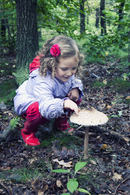 Lächelndes Mädchen berührt einen Pilz, der im Wald wächst, Polen — Stockfoto