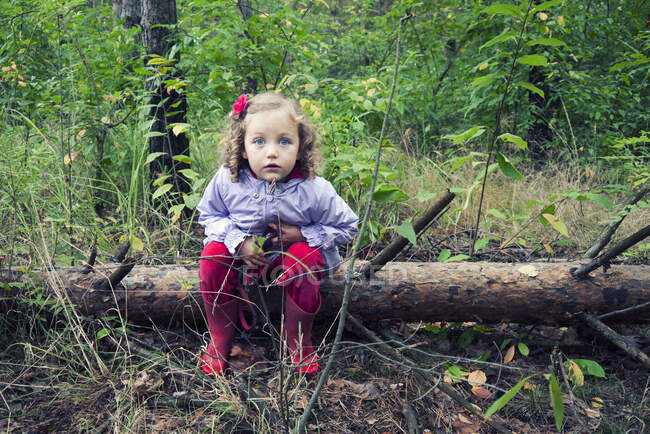 Mädchen sitzt auf einem umgestürzten Baumstamm im Wald, Polen — Stockfoto