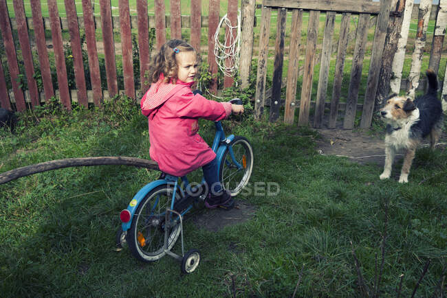 Girl sitting on a bicycle in the garden with her dog, Poland — Stock Photo