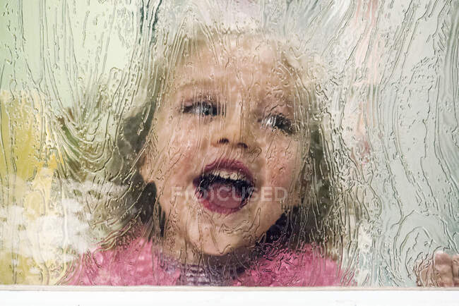 Retrato de una chica de pie detrás de una puerta de cristal riendo - foto de stock