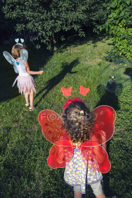 Duas meninas vestindo asas de fada brincando no jardim — Fotografia de Stock