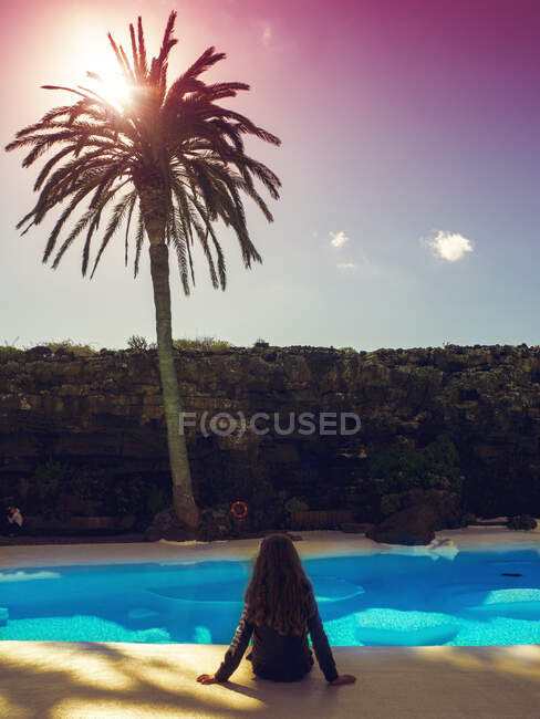 Vista trasera de una chica sentada en el borde de una piscina - foto de stock