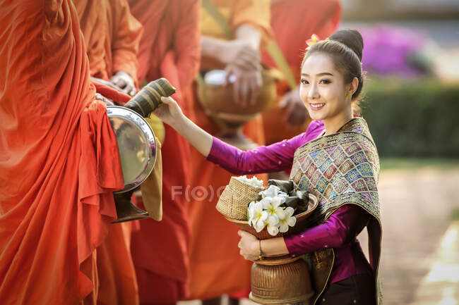 Жінка стає навколішки перед трьома монахами, які пропонують милостиню (Таїланд). — стокове фото