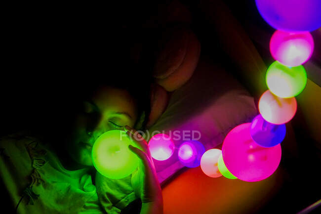Mädchen liegt schlafend im Bett unter bunten Lichtern — Stockfoto