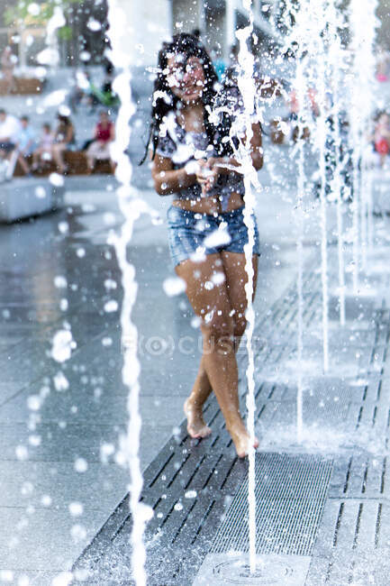 Chica sonriente jugando en una fuente de agua en la plaza de la ciudad, Bulgaria - foto de stock