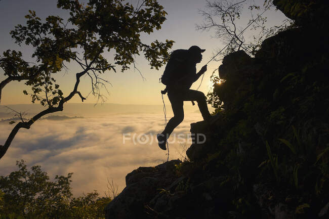 Silhouette of a man rock climbing above cloud carpet, Thailand — Stock Photo