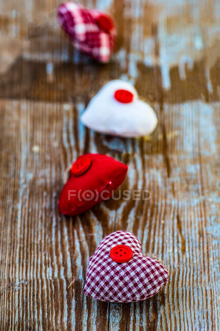 Four ornamental fabric hearts in a row on a wooden table — Stock Photo