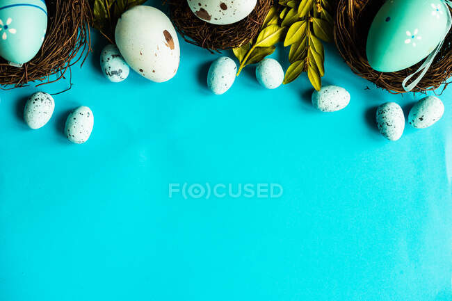Раскрашенные пасхальные яйца и украшения птичьих гнезд на синем фоне — стоковое фото