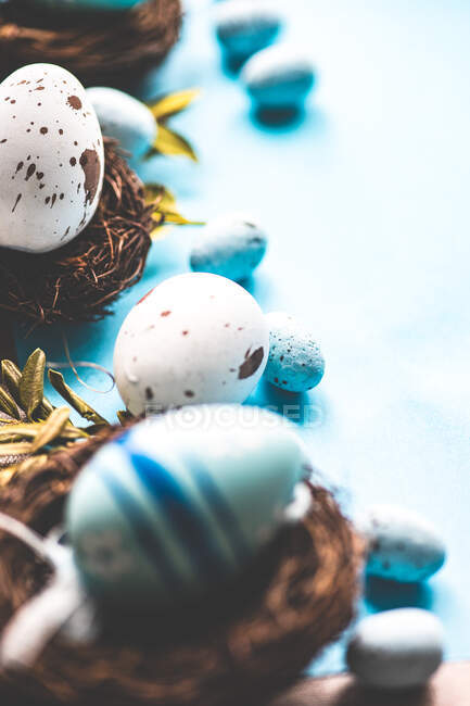 Розфарбовані великодні яйця і пташині гнізда прикраси на синьому фоні — стокове фото