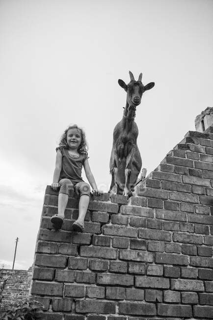 Улыбающаяся девочка, сидящая на стене рядом с козой, Польша — стоковое фото