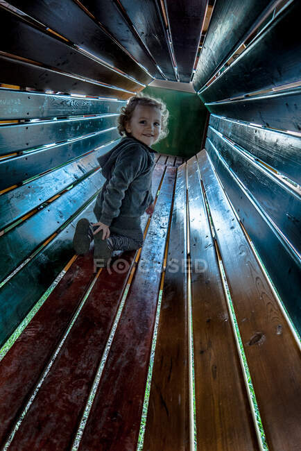 Chica sonriente jugando en un túnel en un parque infantil, Italia - foto de stock