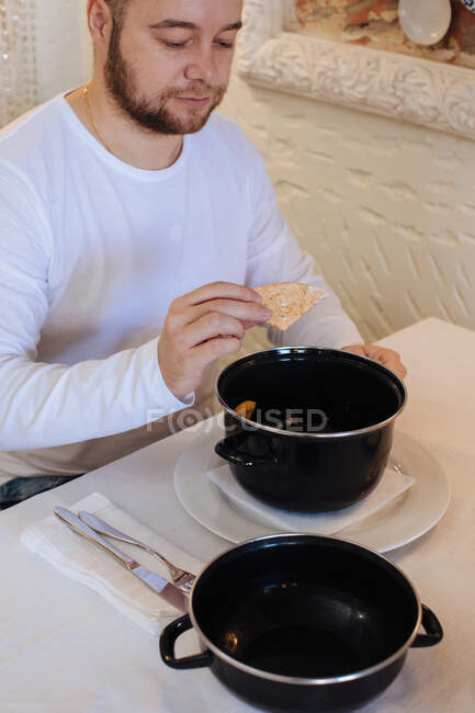 Man eating steamed mussels with a piece of bread — Stock Photo