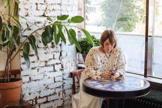 Mulher sentada em um café olhando para seu telefone celular — Fotografia de Stock