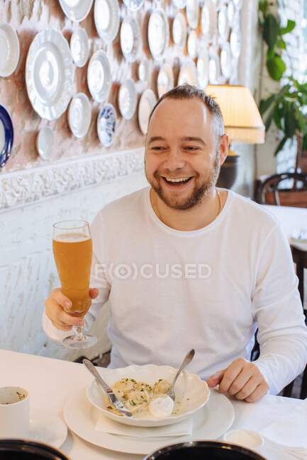 Усміхнений чоловік сидить у ресторані, вечеряє та п'є пиво — стокове фото