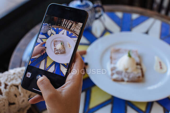 Donna seduta in un caffè a scattare una foto di strudel con gelato — Foto stock