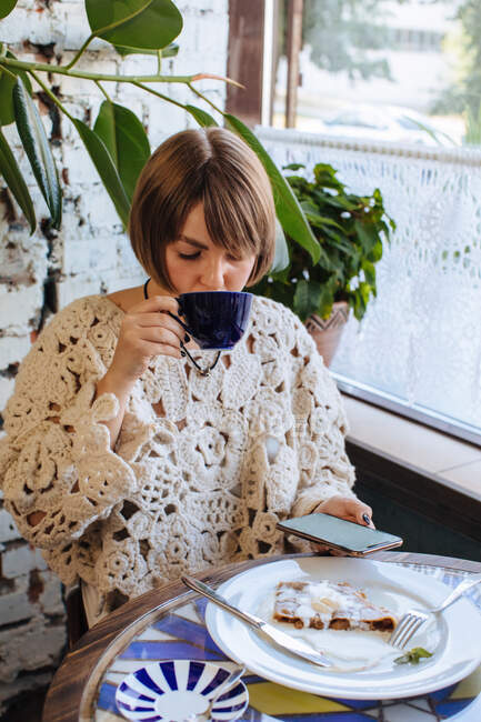 Mujer sentada en un café bebiendo café y mirando su teléfono móvil - foto de stock